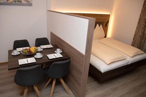 Quarto de hotel com cama, mesa de jantar com cadeiras e uma cesta de frutas.
