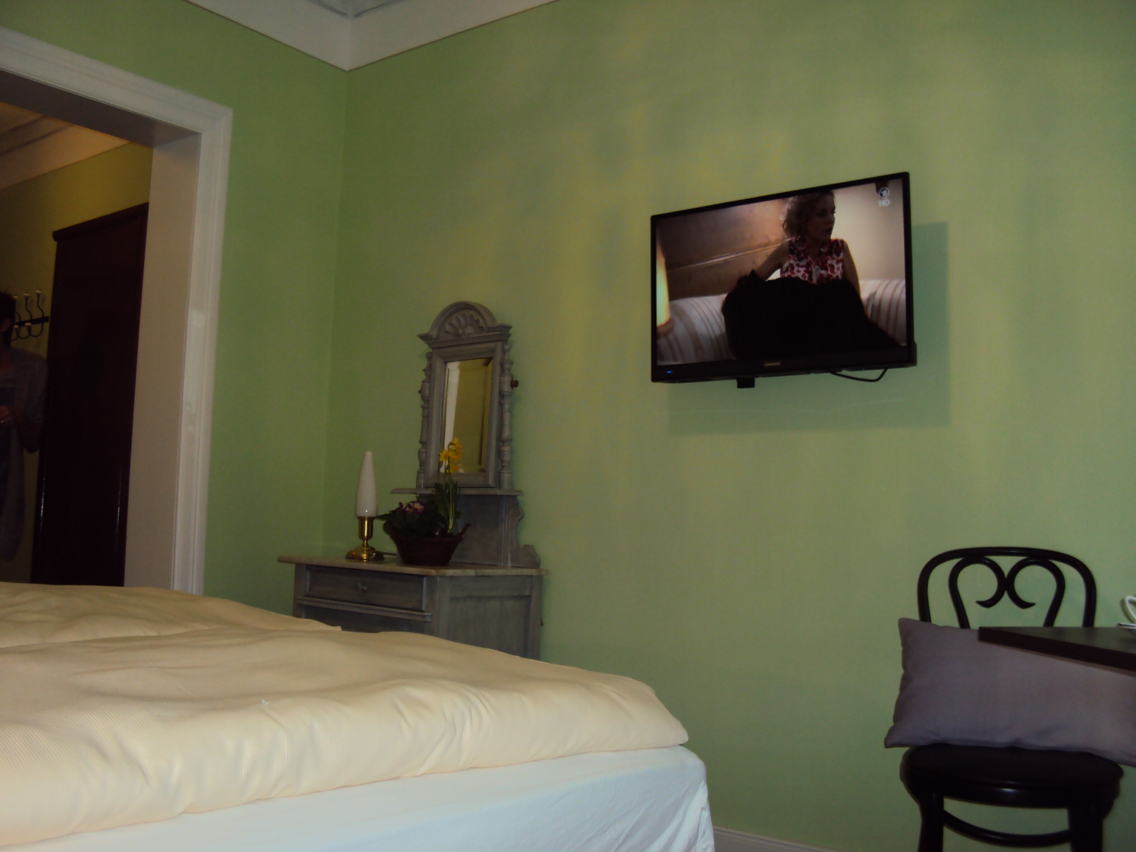 Ein Schlafzimmer mit einem Bett, einem Schminktisch, einem Spiegel und einem an der Wand befestigten Fernseher.