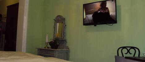 Un dormitorio con cama, cómoda, espejo y televisión montada en la pared.