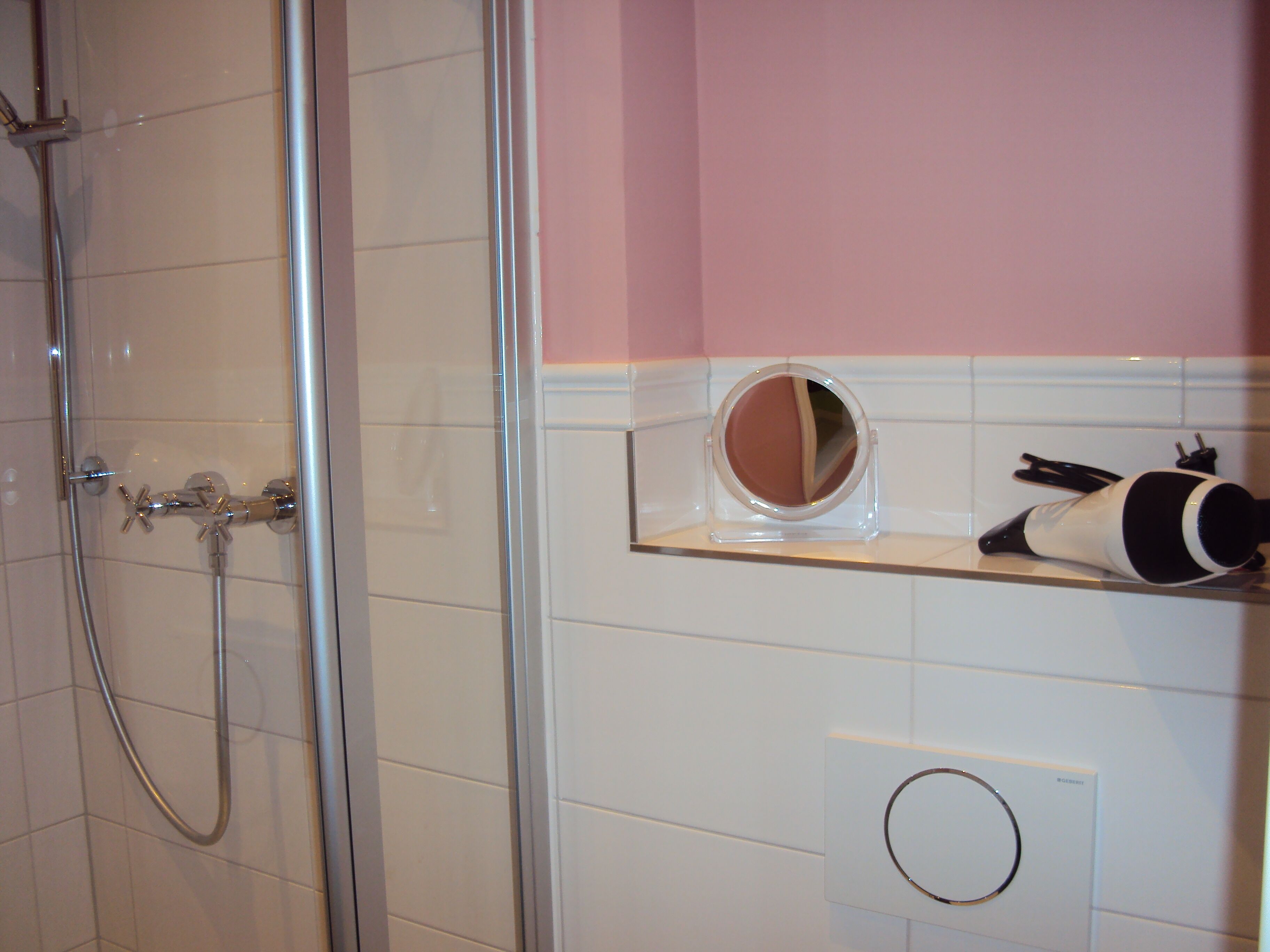 Une salle de bain avec une douche à parois de verre, un meuble-lavabo avec un miroir et un sèche-cheveux posé sur une étagère.
