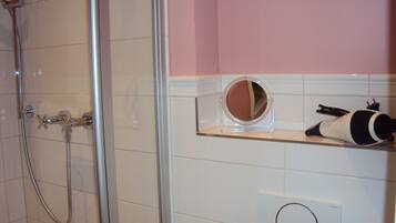 Une salle de bain avec une douche à parois de verre, un meuble-lavabo avec un miroir et un sèche-cheveux posé sur une étagère.