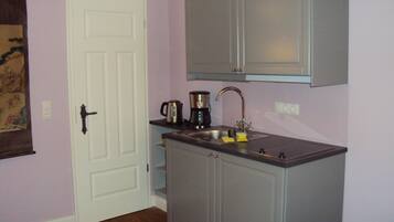 A compact kitchen with a white door, a coffee maker, and a sink.