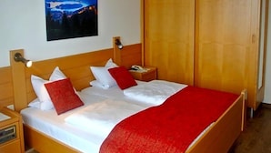 A hotel room with a wooden bed, a nightstand, a red throw blanket, a wooden wardrobe, and a night light. - Baumgartnerhof (Finkenstein am Faaker See)