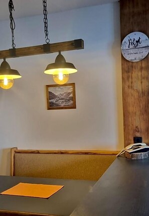 A dining area with a wooden bench, a table with a placemat, pendant lights, a framed picture on the wall, and a clock. - Baumgartnerhof (Finkenstein am Faaker See)