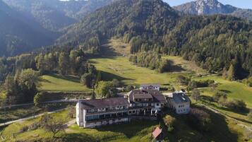 Un grand bâtiment doté de nombreuses pièces, entouré de champs verdoyants et de collines boisées.