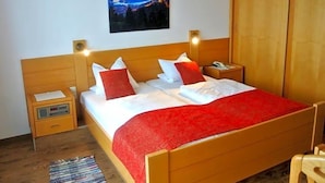 A bedroom with a wooden bed, a nightstand, a bedside table, a red throw blanket, a wall-mounted lamp, and a framed picture. - Baumgartnerhof (Finkenstein am Faaker See)