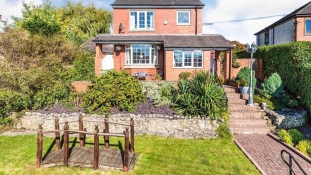 A two-story house with a brick exterior, a front porch, and a garden with a wooden bridge.