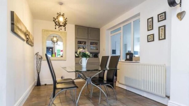 A dining area with a glass table and metal chairs, a chandelier, and a view of the kitchen through an archway. - Higherlands (Stoke-on-Trent)
