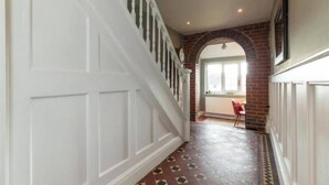 A hallway with a white door, a staircase with white balusters, and a brick archway leading to a room with a window.