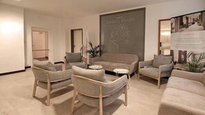 A modern interior with a sofa, armchairs, a small table, and a wall with a logo. - Harvey SPA & KUR (Frantiskovy Lazne)
