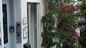 Un étroit couloir extérieur agrémenté de plantes en pot et muni d’une porte sur laquelle est apposée une pancarte.