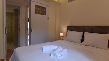 Habitación de hotel con una cama bien hecha, una puerta que da al baño y una mesita de noche pequeña con una lámpara.