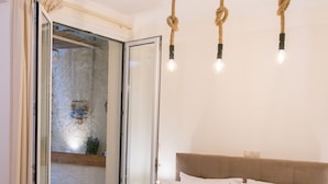 Un lit bien fait, avec du linge de lit blanc et une serviette pliée, une tête de lit en bois et une porte en verre donnant sur un espace extérieur.