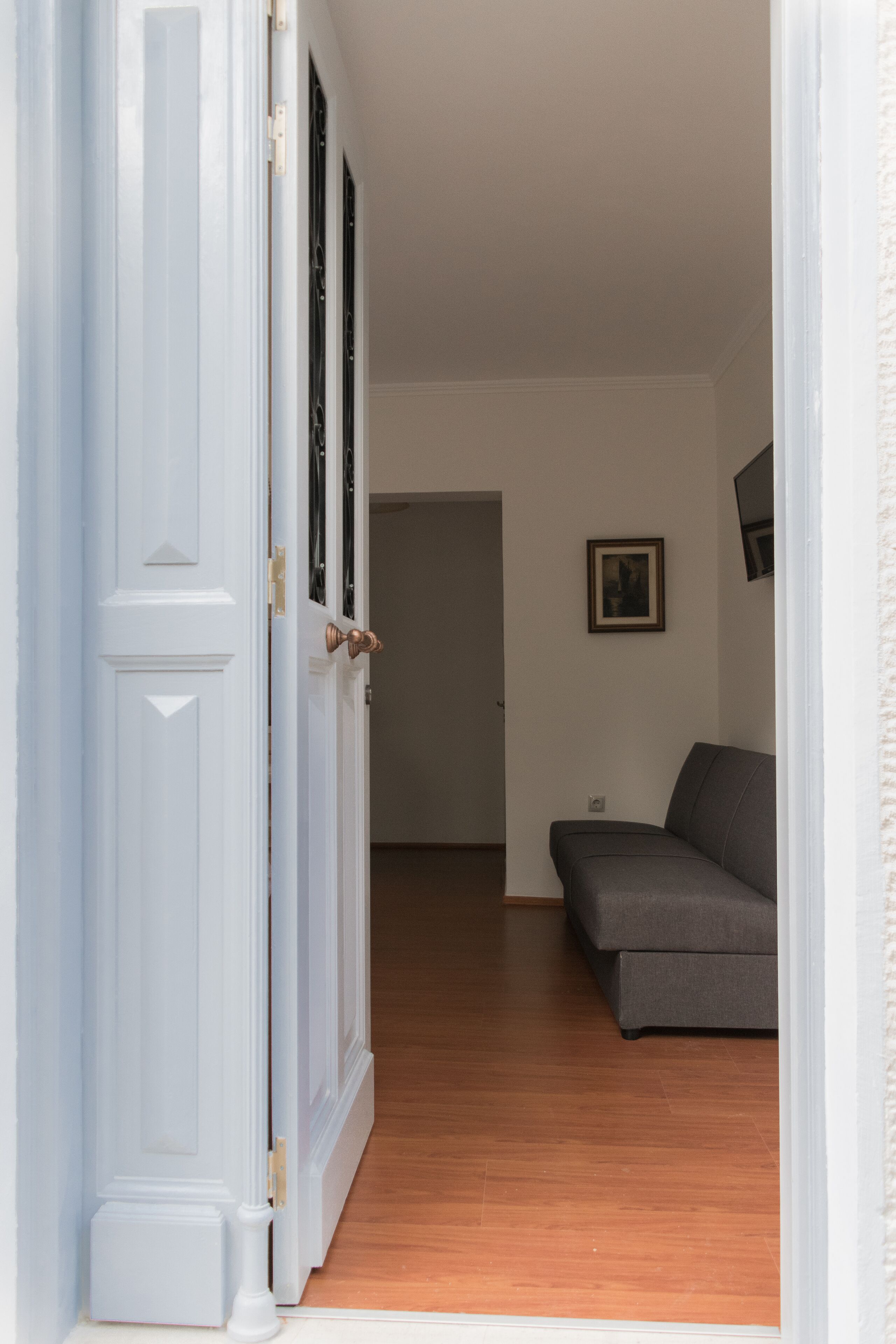 An open door leading to a room with a grey sofa, wooden flooring, and a framed picture on the wall.