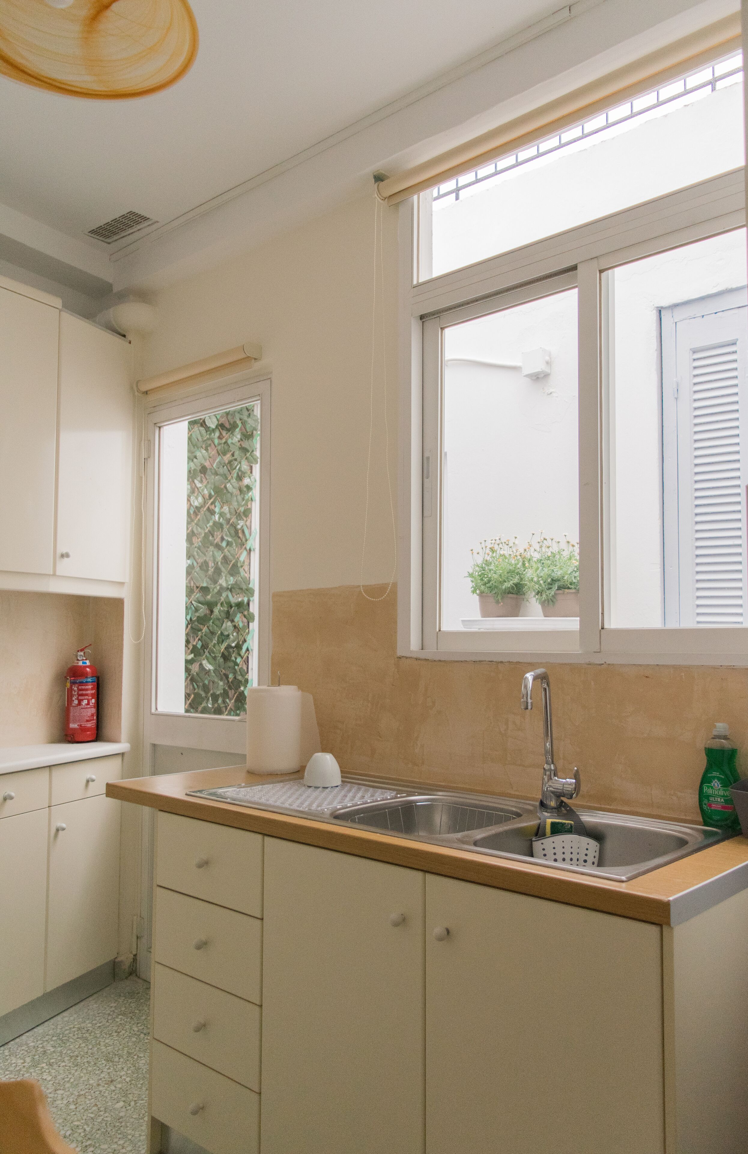 Una cocina con dos fregaderos, una ventana con persianas y un extintor en la encimera.