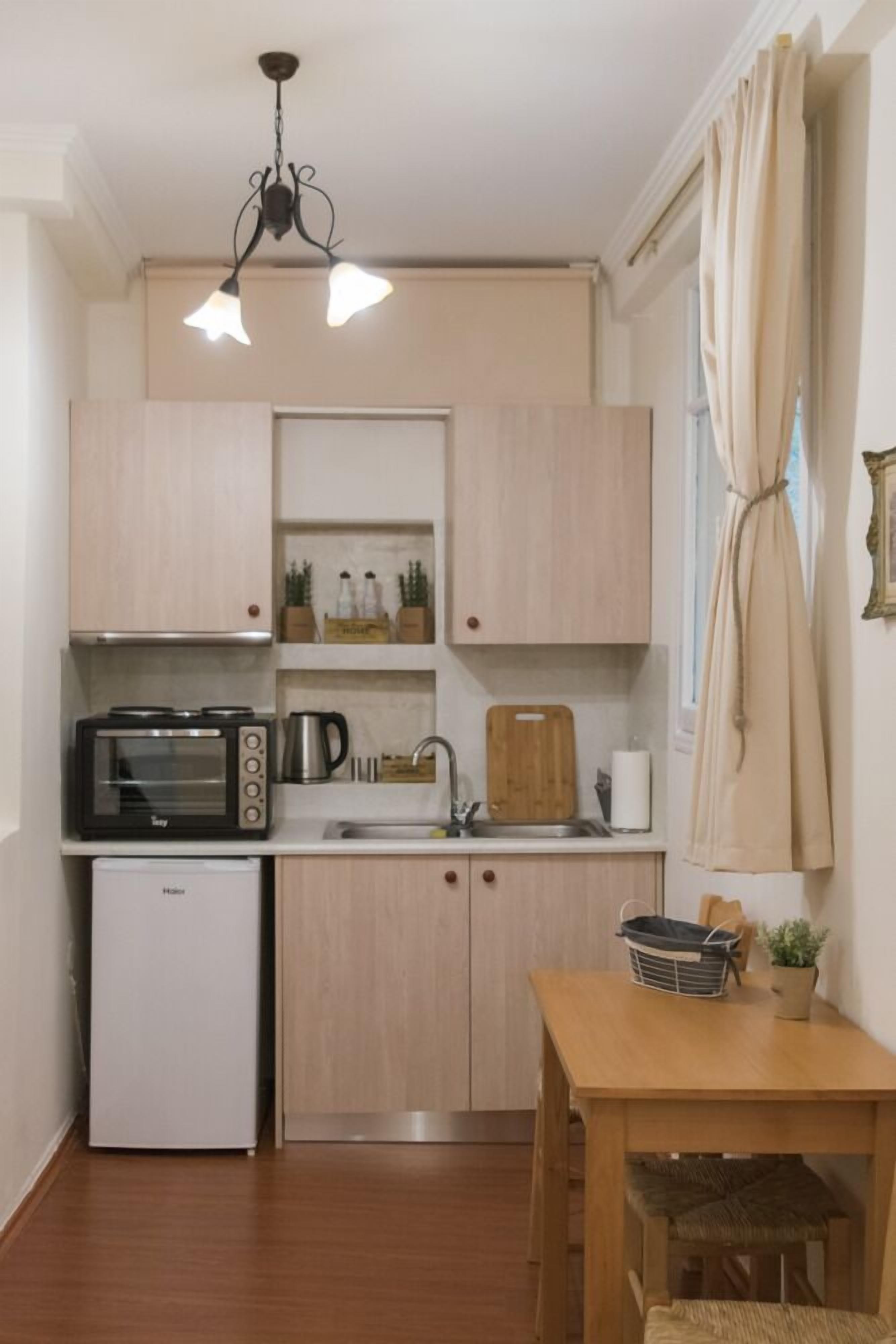 A compact kitchen with a microwave, toaster, and refrigerator. There is a wooden table with chairs and a small potted plant.
