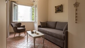 Un salon avec un canapé, un fauteuil, une petite table et une fenêtre avec des rideaux.