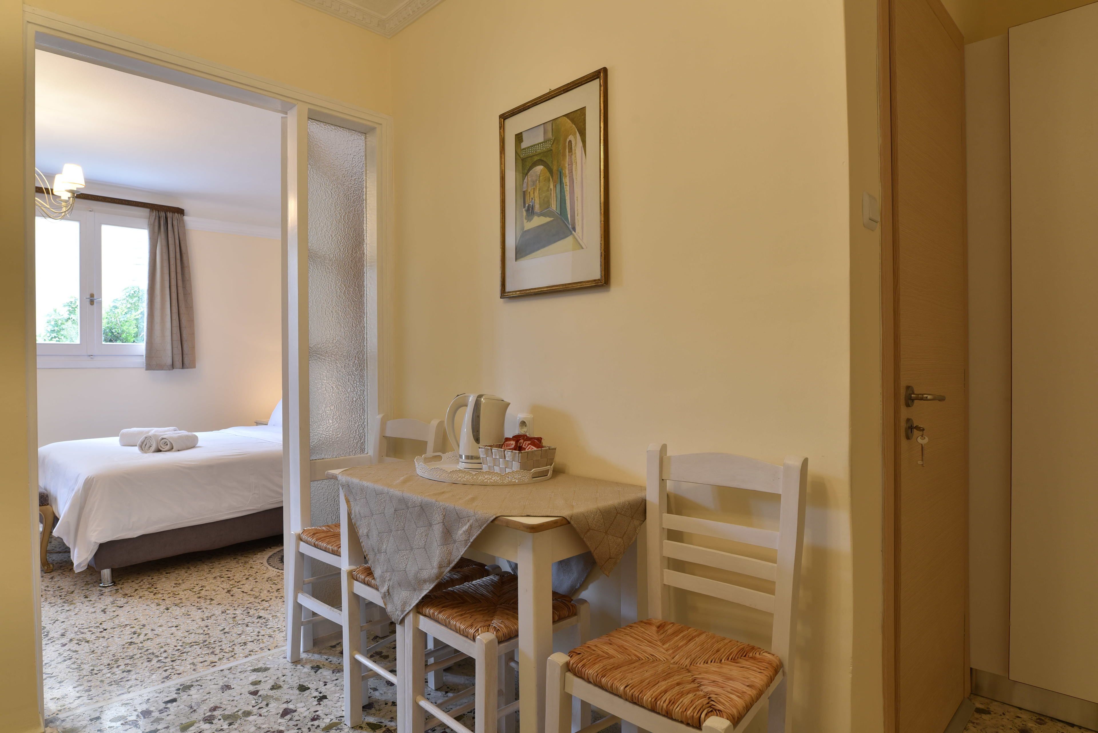 Una camera d'albergo con un letto, un tavolo da pranzo con sedie, un quadro appeso al muro e una porta.