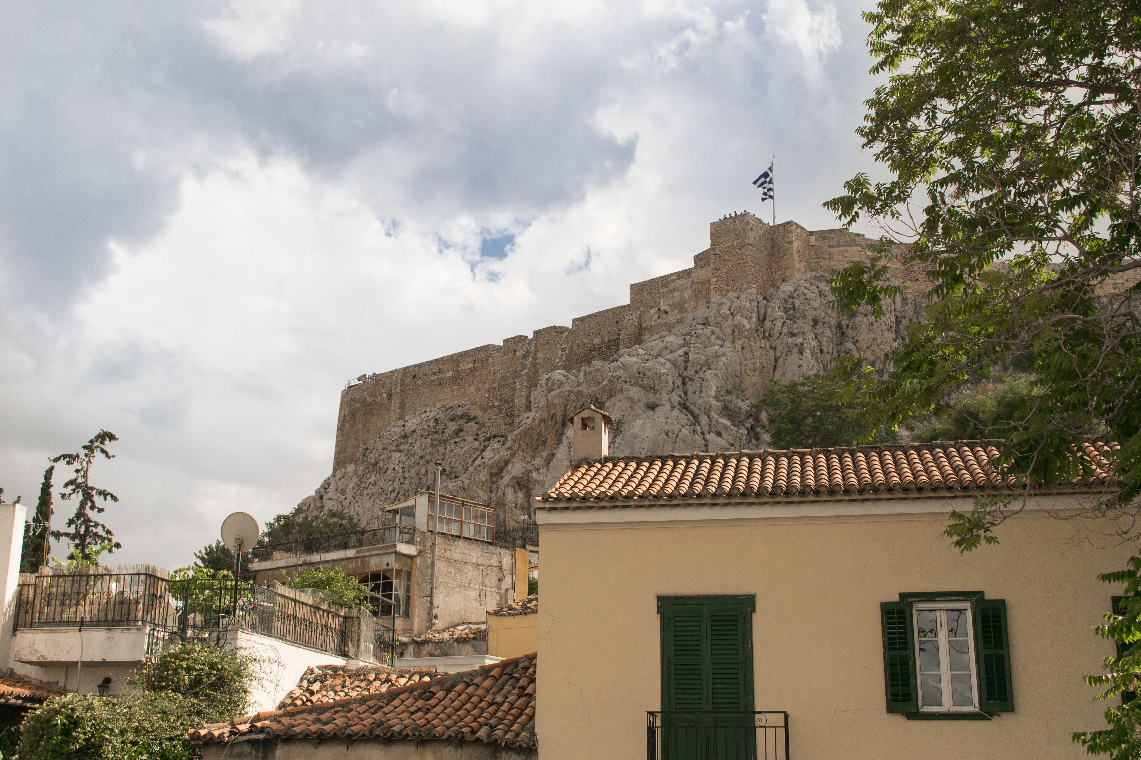 Una fortaleza de piedra histórica con tejado de tejas y una bandera, con vistas a un pueblo de edificios tradicionales y cielo despejado.