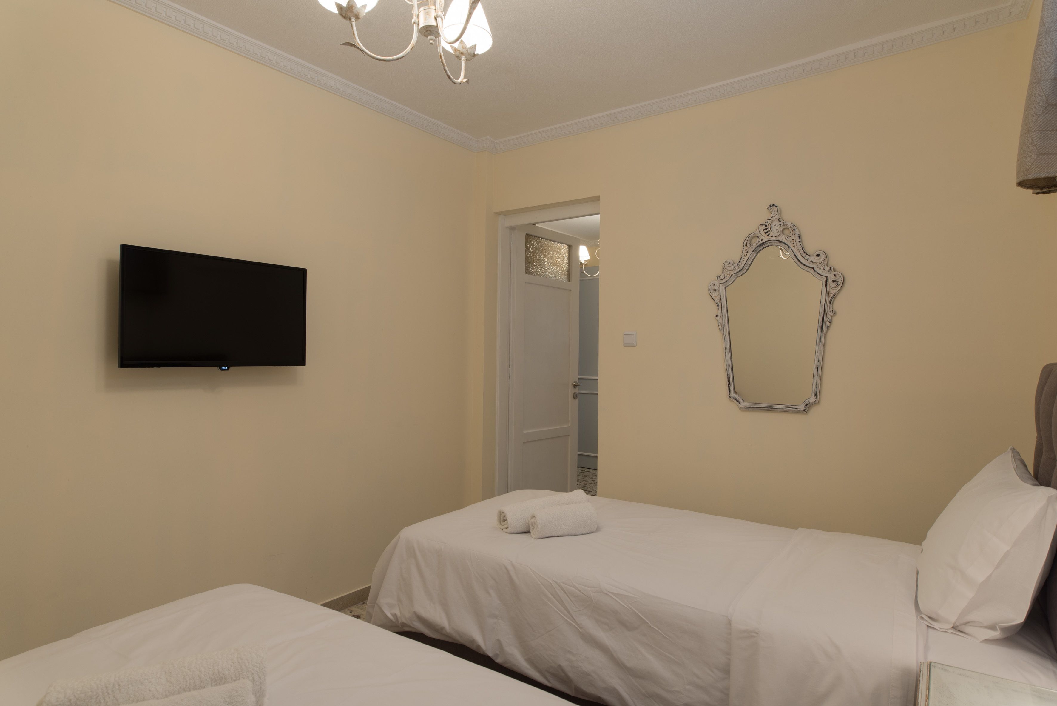 A hotel room with two beds, a flat-screen TV, a decorative mirror, and a chandelier.