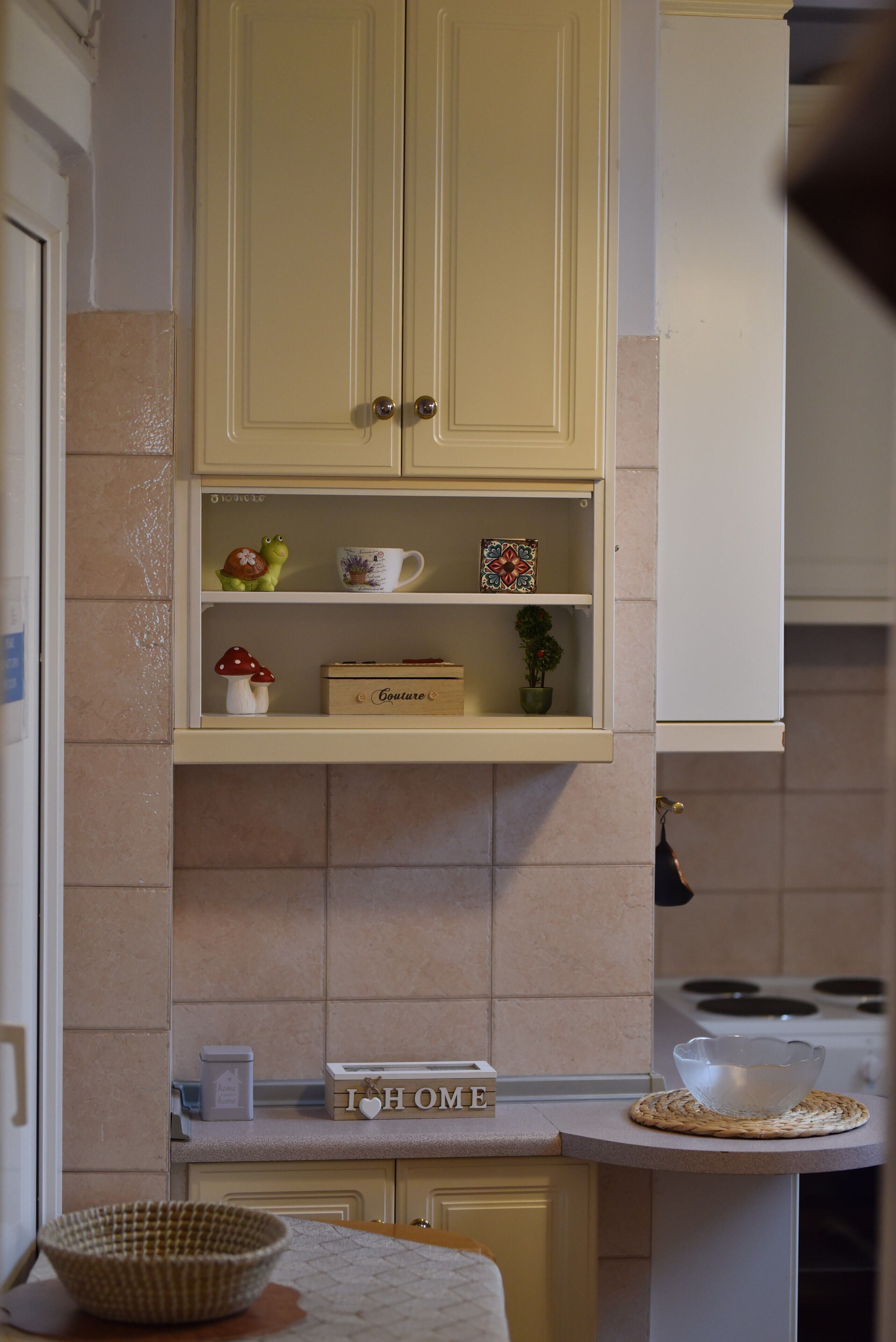 Eine Küche mit hellgelben Schränken, einer Arbeitsplatte mit Schüssel, Kaffeetasse und einem dekorativen Schild mit der Aufschrift 'I   ♥ HOME'.