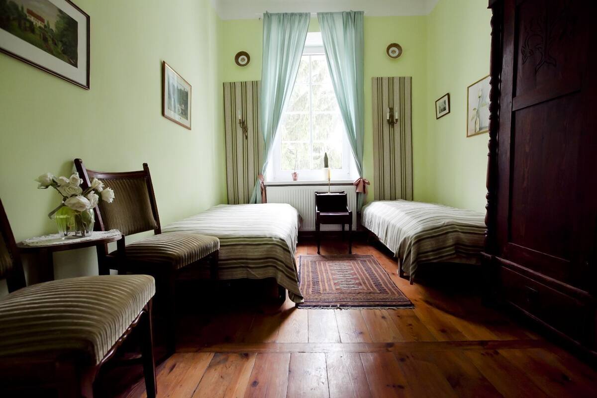 Ein Zimmer mit zwei Einzelbetten, Holzboden, einem kleinen Tisch mit Blumenvase und einem Stuhl.