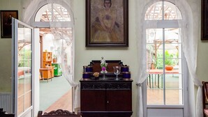 A room with a wooden cabinet, a framed painting, and two arched windows with curtains. - Dwor W Odonowie (Kazimierza Wielka)