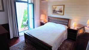 Une chambre avec un grand lit, deux tables de chevet avec des lampes, un tableau au mur et une vue à travers une porte vitrée.
