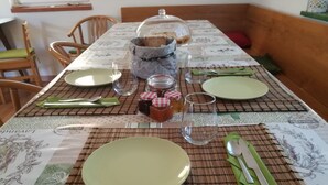 Une table à manger dressée avec des assiettes, des couverts et un pichet en verre, le tout recouvert d’une nappe à motifs floraux.
