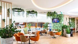 A modern indoor space with wooden flooring, orange and beige chairs, and hanging plants. - Hotel Ba Antowo Sport (Katowice)