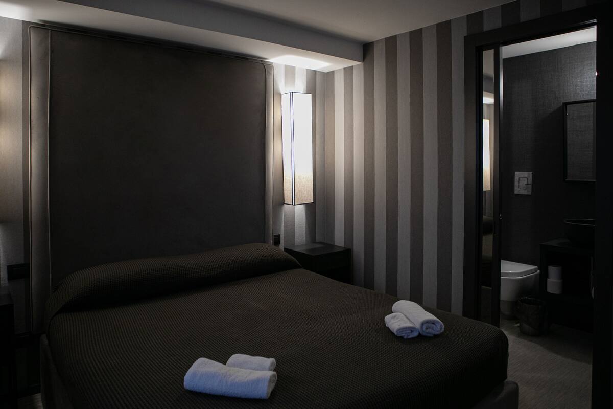 A hotel room with a large bed, a nightstand, a lamp, and a door leading to a bathroom.