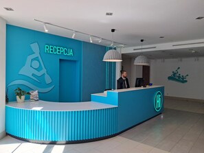A reception desk with a blue color scheme and a logo, a man standing behind it, and a wall with a kayak graphic. - Hotel Kolna (Kraków)