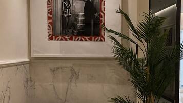A lobby area with a marble floor, a grey sofa, a potted plant, and a framed picture on the wall.