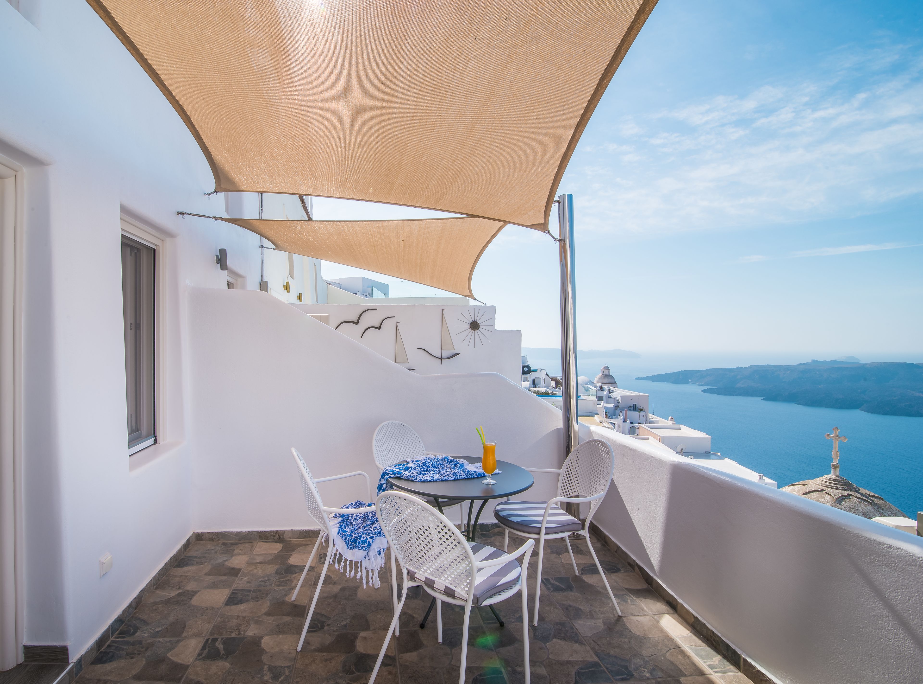 Ein Balkon mit weißen Wänden, einem Tisch, Stühlen und Blick aufs Meer.