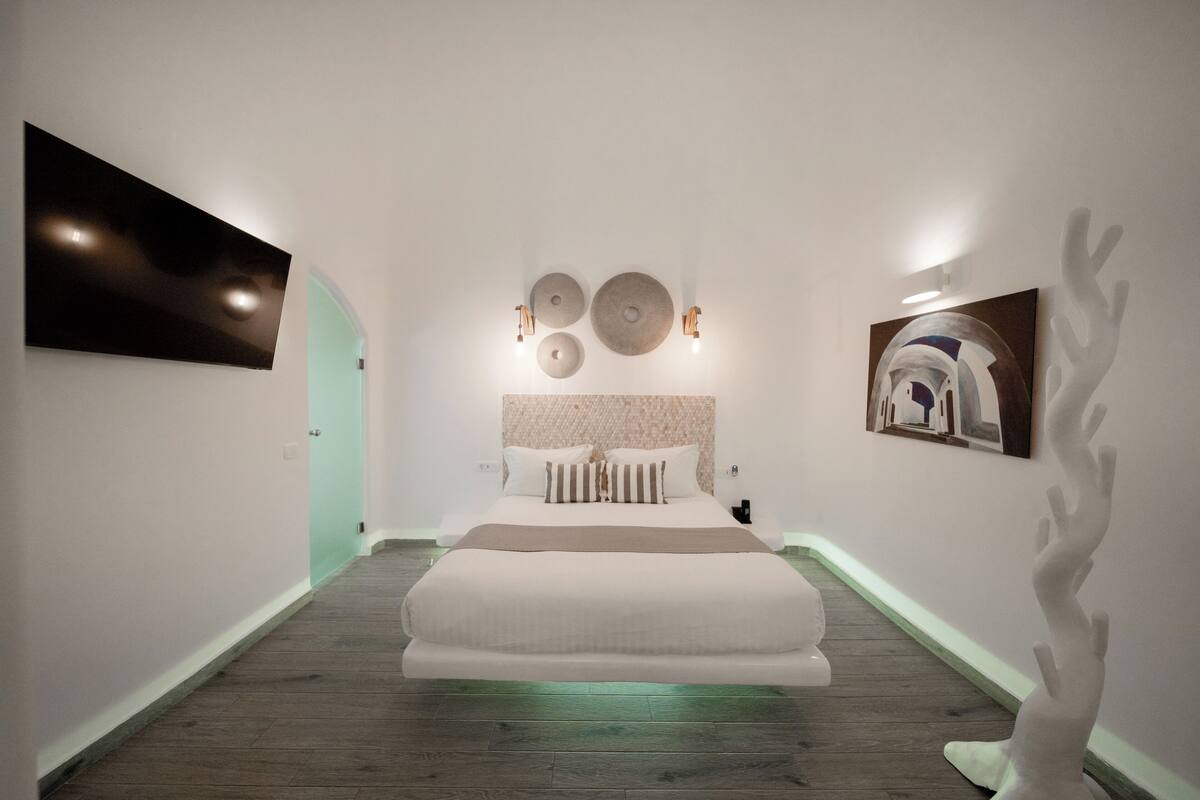 A modern bedroom with a large bed, a wall-mounted TV, and decorative wall art.