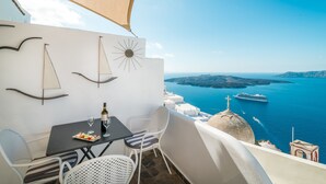 A balcony with a table, chairs, and a bottle of wine. The view includes a ship and the sea. - Angel Luxury Suites (Santorini)