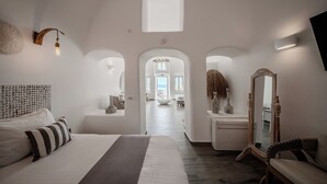 A hotel room with a large bed, a mirror, a wall-mounted light fixture, and an arched doorway leading to a balcony. - Angel Luxury Suites (Santorini)