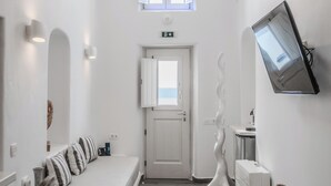 A minimalist room with a sofa, a wooden table, a TV mounted on the wall, and a door leading to another room. - Angel Luxury Suites (Santorini)