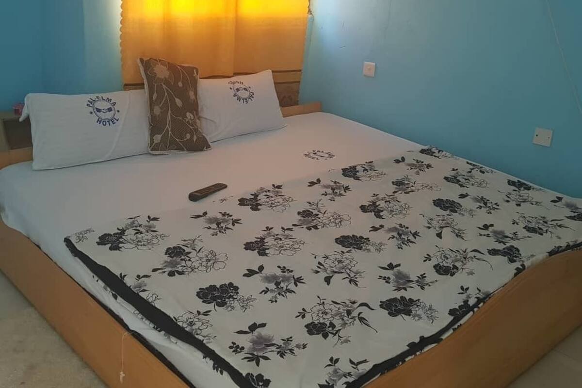 A bed with a floral bedspread, a pillow with a logo, and a remote control on it.