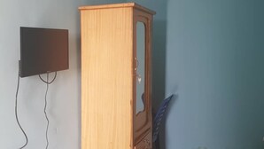 Una habitación con un armario de madera, un televisor de pantalla plana montado en la pared y una silla de plástico.