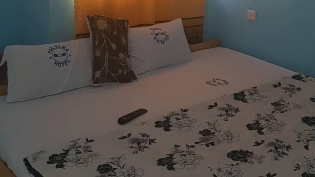 Una habitación con una cama, dos almohadas, un control remoto y un aire acondicionado instalado en la pared.