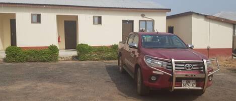 A red Toyota Hilux parked in front of a building with a white and red facade, a small window, and a door.