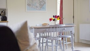 A dining area with a white table and chairs, a map on the wall, and a vase with flowers. - Fig Cottage (Eastbourne)