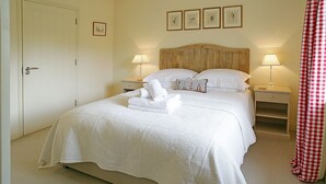 A neatly made bed with white linens and a folded towel, two bedside tables with lamps, a wooden headboard, and a door. - Fig Cottage (Eastbourne)