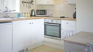 A compact kitchen with white cabinets, a microwave, an oven, a sink, and a window. - Fig Cottage (Eastbourne)