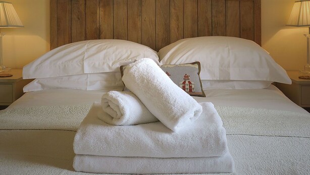 A neatly made bed with white linens, a wooden headboard, and a pillow with a lighthouse design. There are four framed pictures on the wall above the bed. - Fig Cottage (Eastbourne)
