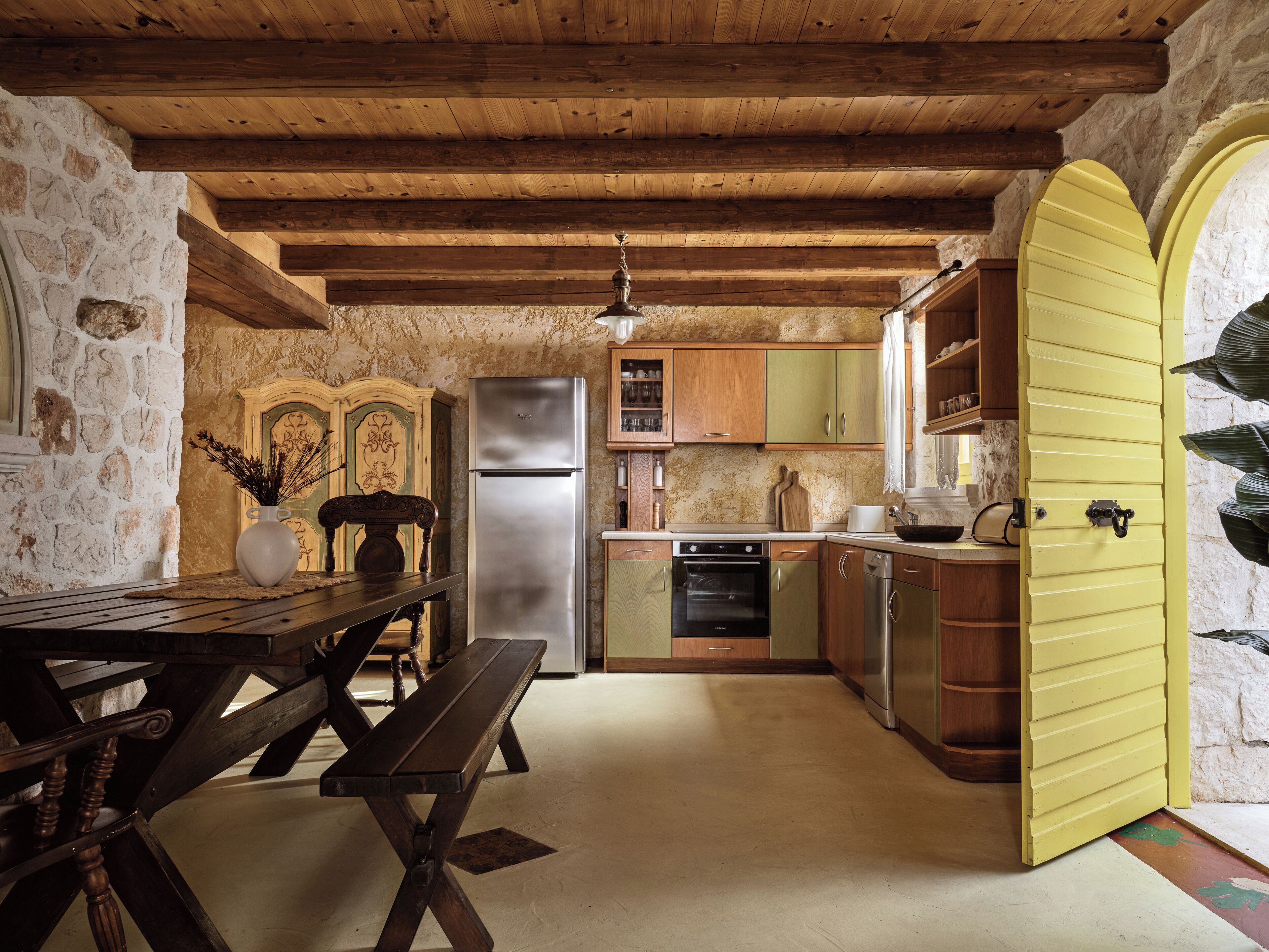Une cuisine rustique avec une table et un banc en bois, un réfrigérateur et une porte jaune.