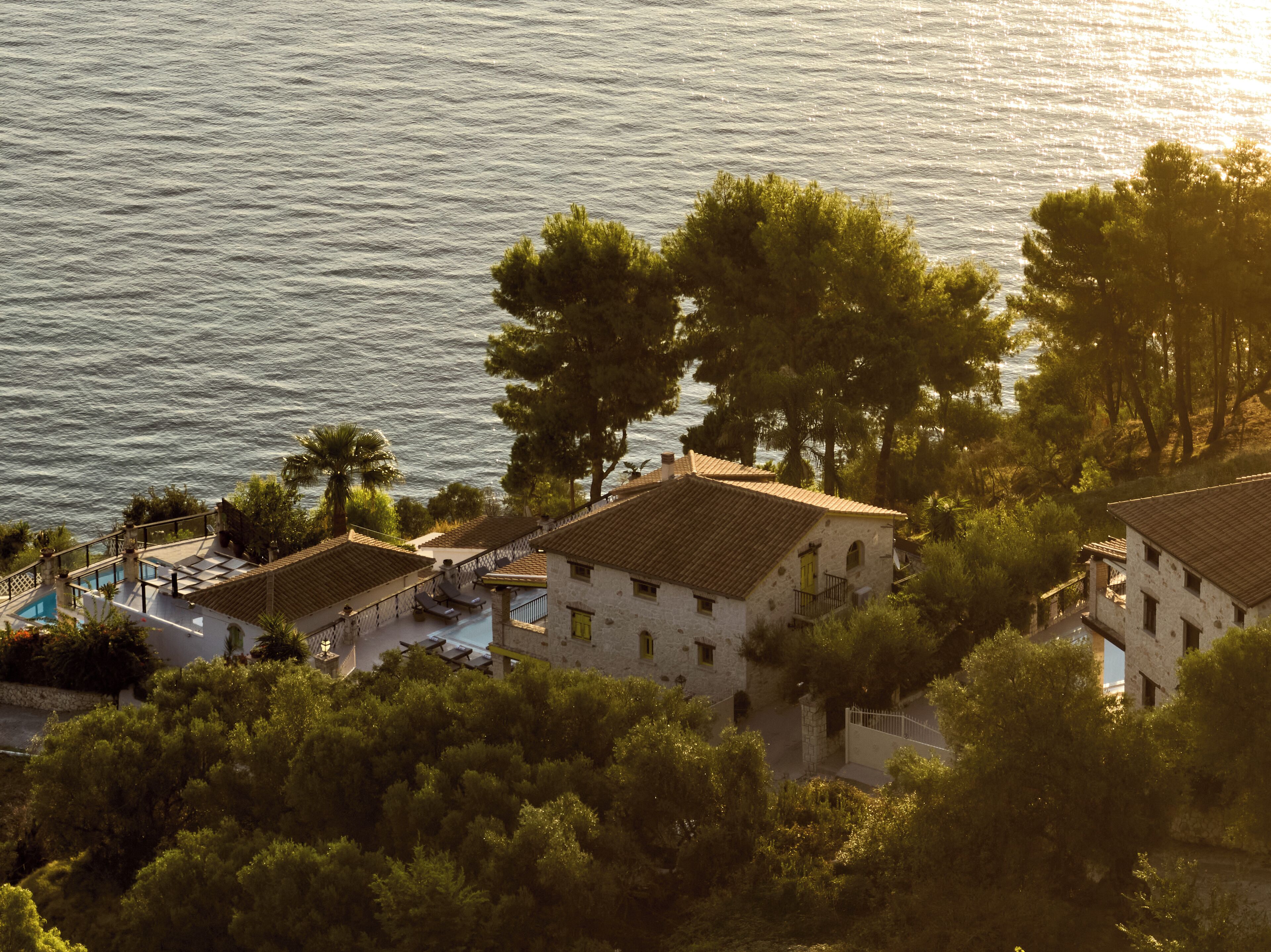 En villa vid kusten med en pool, omgiven av träd och med utsikt över havet.
