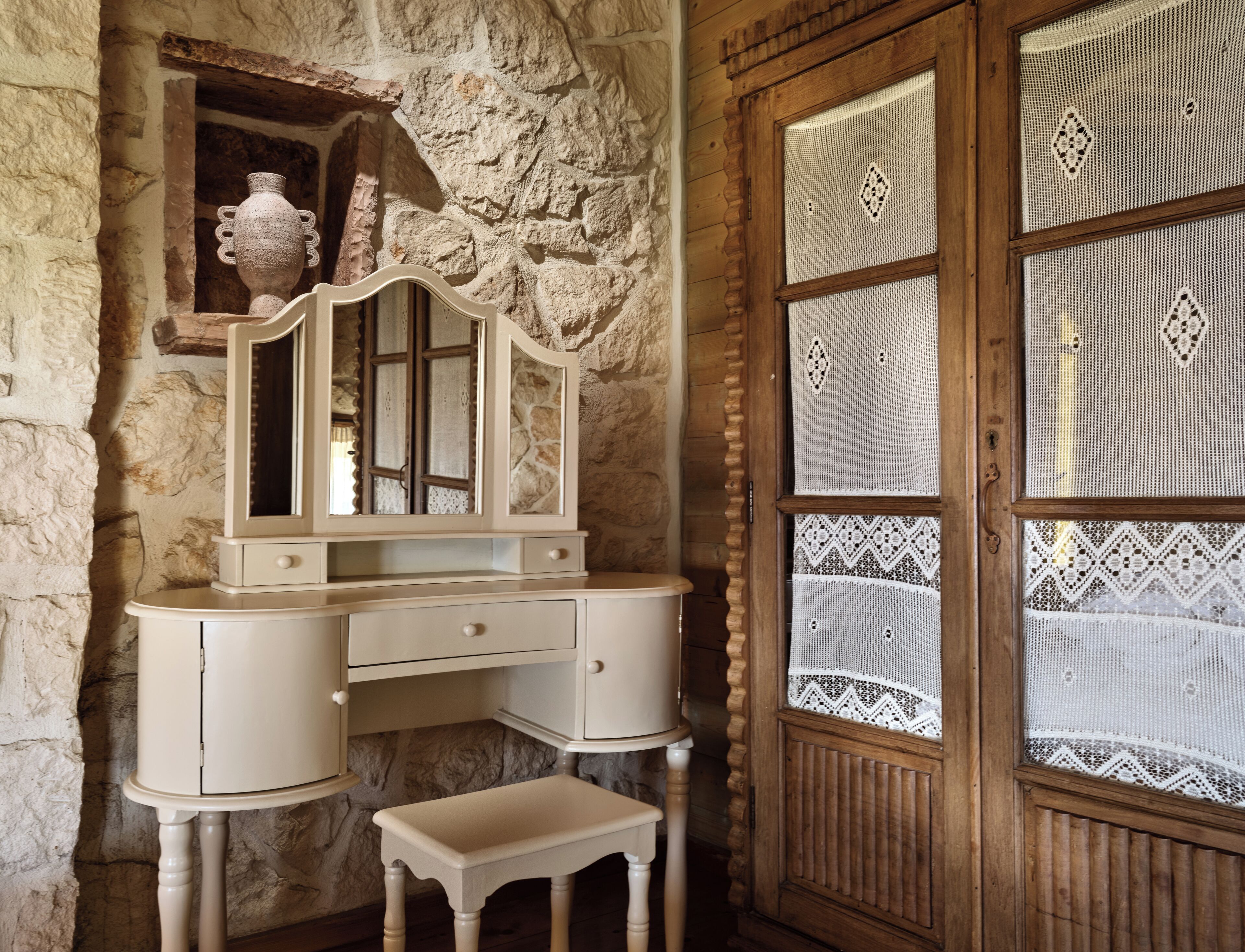 A stone wall with a wooden vanity and a lace-covered window.