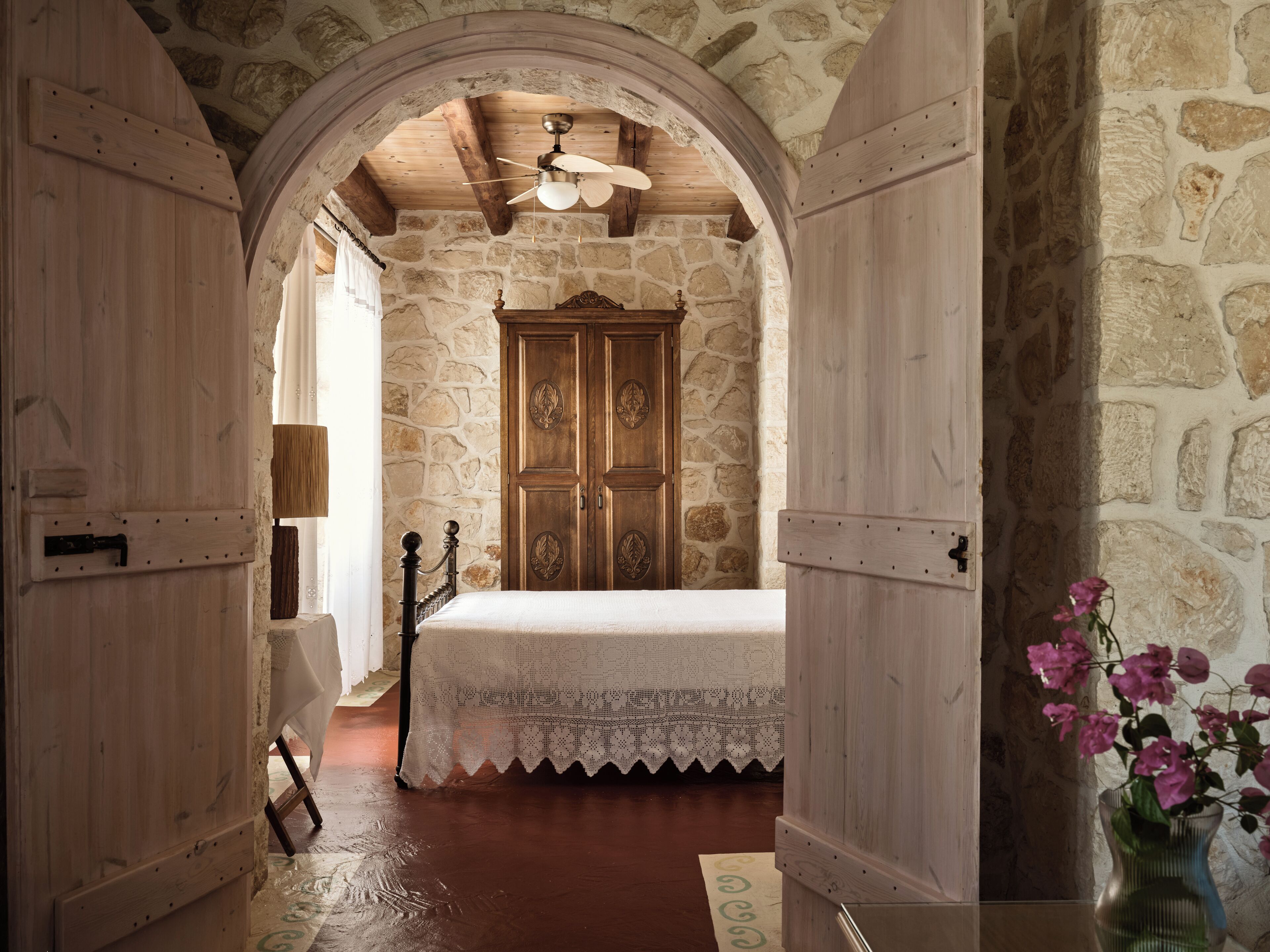 A bedroom with a stone wall, wooden door, and a bed with a white bedspread.